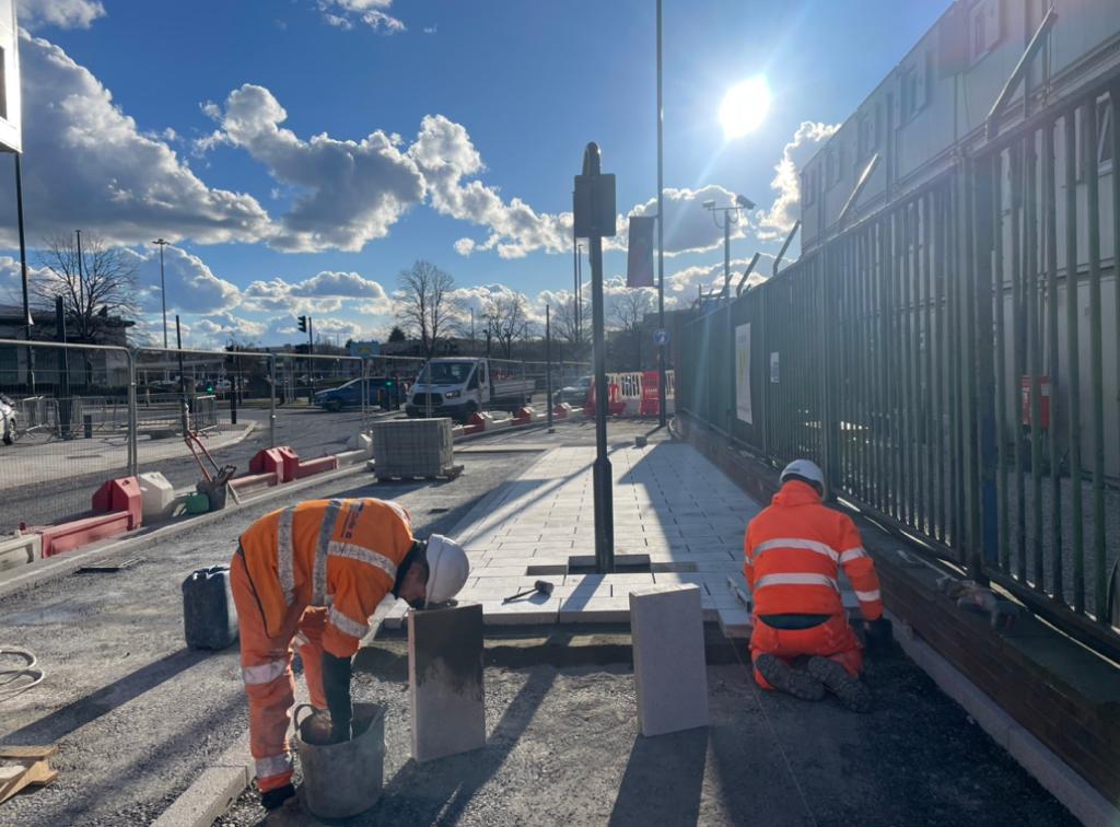 Two builders wearing orange high-vis outfits laying pavement blocks down