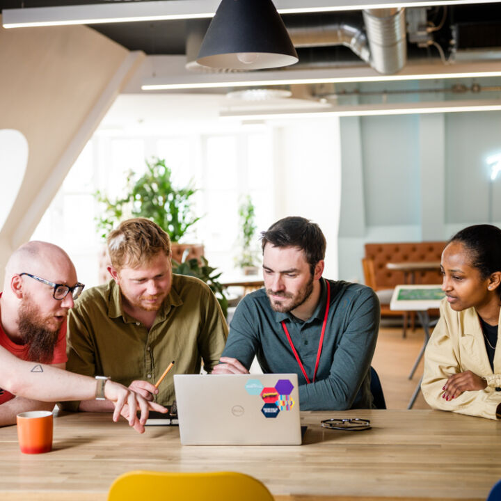 Three men and a woman looking, talking and pointing at a laptop together