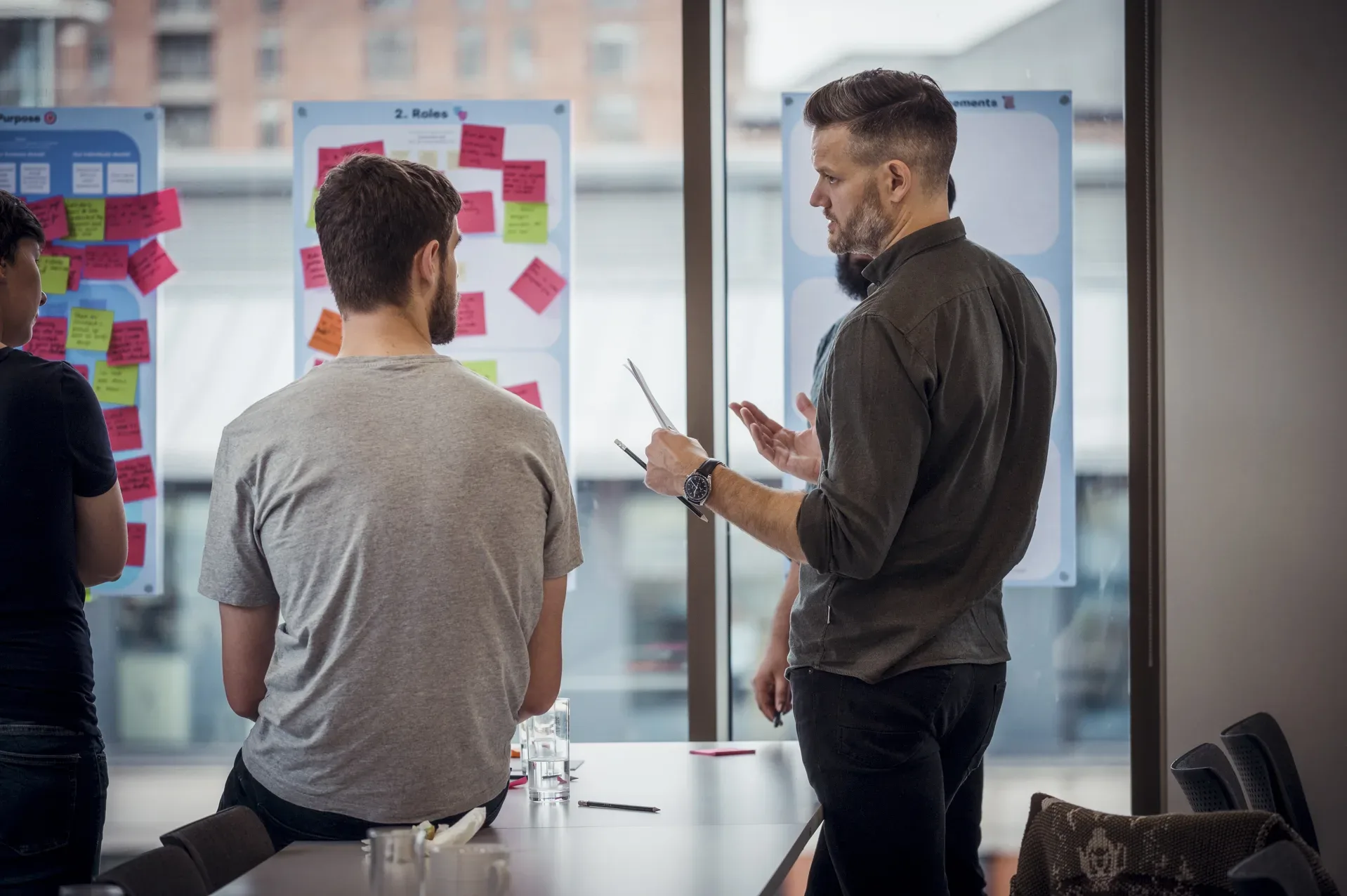Two men talking together in front of poster boards with sticky notes of ideas.