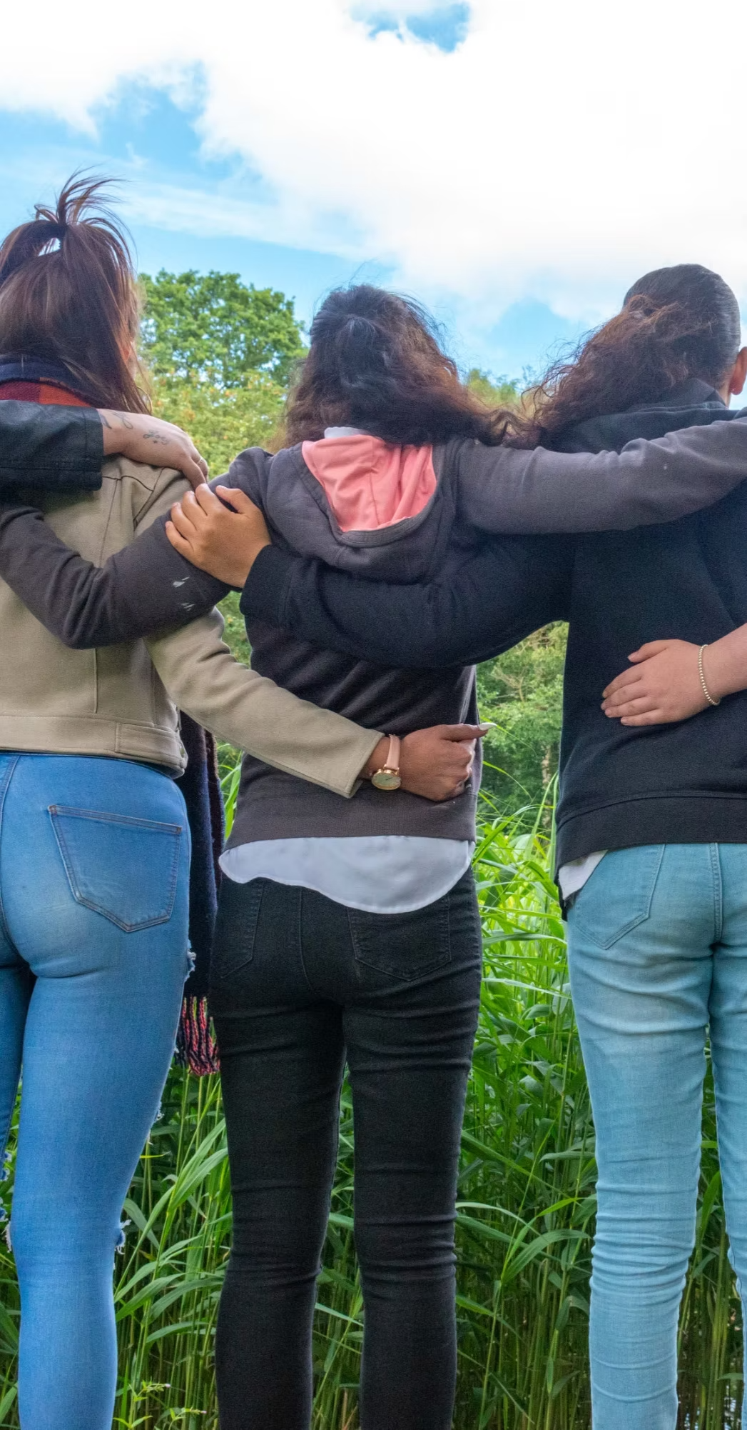 A group of women have their arms around one another on a sunny day, they have their backs to the camera
