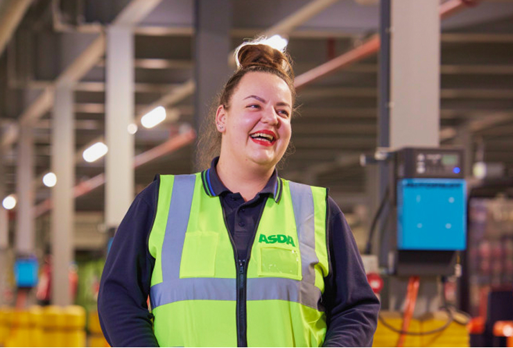 A female staff member is laughing inside a warehouse wearing a high vis ASDA branded jacket