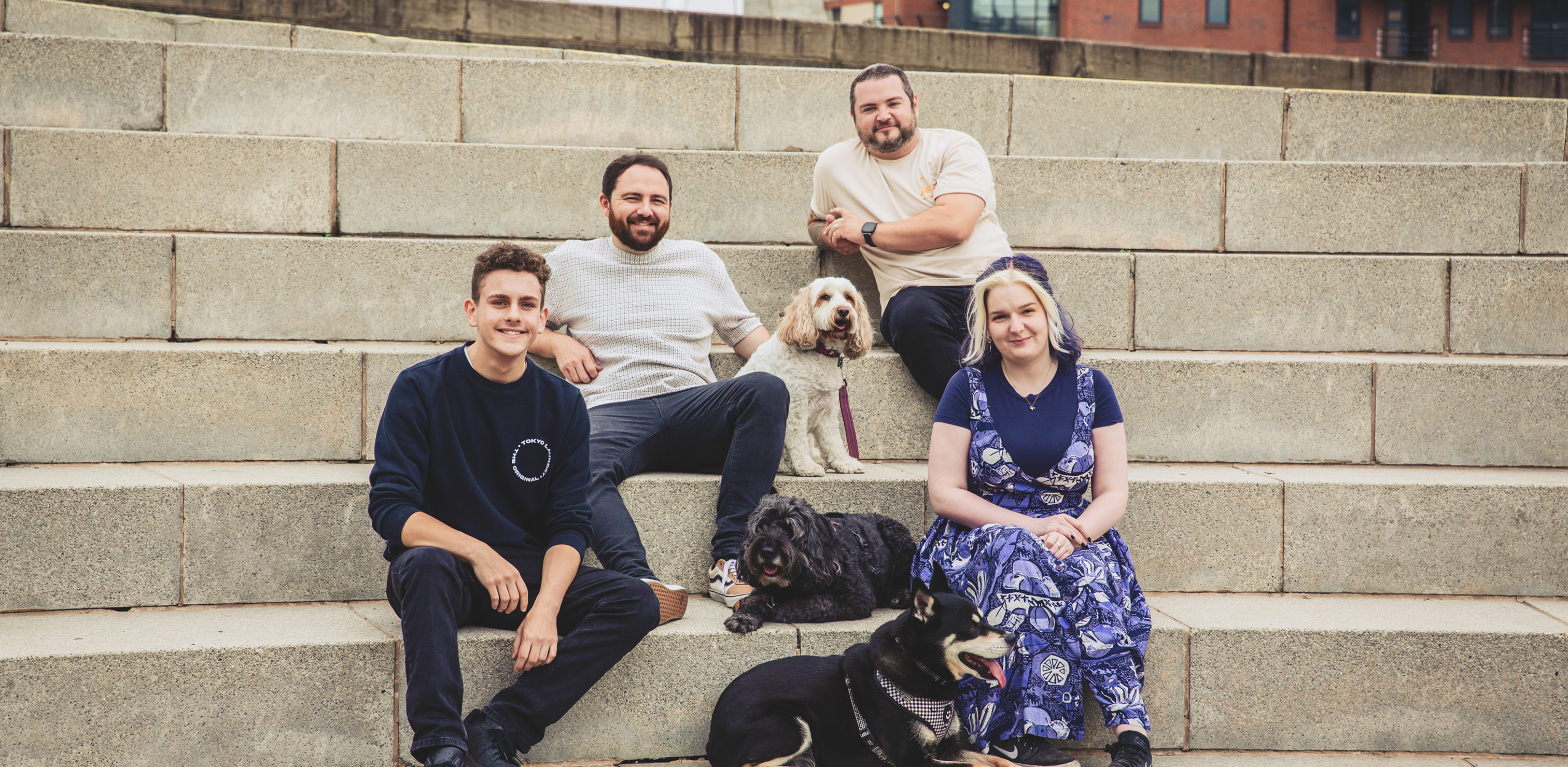 The Few and Far team sit on the steps outside the Royal Armouries in Leeds, 4 team members and 3 dogs pose for the camera